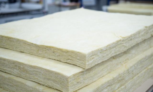 Mantas aislantes de fibra de vidrio apiladas en un taller industrial con luz suave